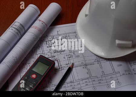 Lasermeter, weißer Hardhat und Zeichnungen am Ingenieurarbeitsplatz. Stockfoto