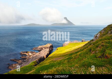 Morgenblick auf die Färöer Insel Koltur mit spektakulären Wolken und blauem Wasser in einem dramatischen Tal mit Bergkette. Färöer, Dänemark. Landschaftsfotografie Stockfoto