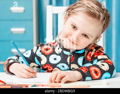 Charmante blonde kleine Mädchen mit schönen Augen zeichnet mit Bleistiften und schaut auf die Kamera Stockfoto