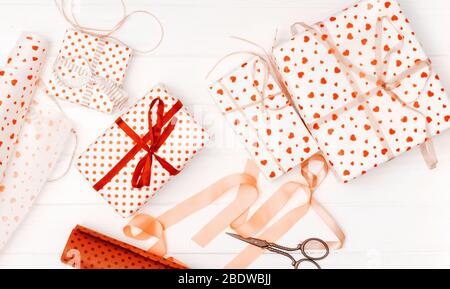 Flaches Ley von kleinen Geschenken in gemusterten Herzen Geschenkpapier, Schere und Seidenband verpackt Stockfoto