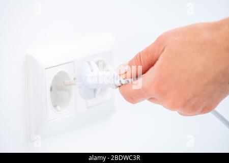 Kabel von Hand in die Buchse an der weißen Wand stecken Stockfoto