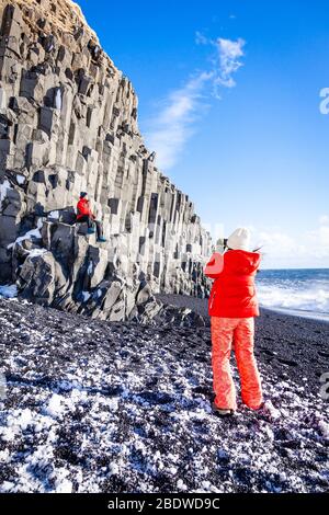 Touristen fotografieren im Winter an Basaltsäulen am schwarzen Sandstrand Reynisfjara in der Nähe von Vík í Mýrdal, Südisland Stockfoto