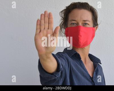 Kaukasische Frau trägt eine hausgemachte DIY Gesichtsmaske und macht die Hand Handfläche Stop-Zeichen während der 2019-20 Corona-Virus Pandemie - bleiben Sie weg. Stockfoto