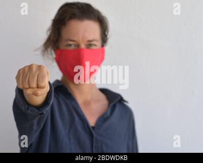 Kaukasierin trägt eine selbstgemachte DIY-Gesichtsmaske und zeigt ihre Faust während der 2019-20 Corona-Virus-Pandemie - Kampf gegen Corona. Stockfoto