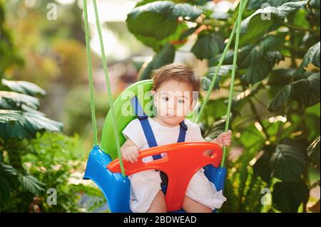 Porträt von Baby Mädchen auf Schaukeln in verschwommenem Garten Hintergrund Stockfoto