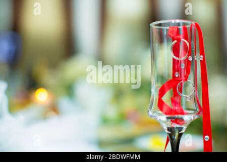 Die Ringe hingen von einem roten Band. Im Hintergrund ein Blumenstrauß für die Hochzeit. Im Glas sind Ringe und Bänder angebracht. Zwei Hochzeitsringe hingen von A. Stockfoto