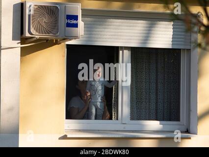 Belgrad, Serbien. April 2020. Die Mutter und das Baby schauen aus dem Fenster ihrer Wohnung während einer Ausgangssperre, die zur Verhinderung der Ausbreitung der Coronavirus-Krankheit (COVID-19) verhängt wurde. Der serbische Präsident Aleksandar Vucic hatte den Ausnahmezustand erklärt, um die Ausbreitung des Coronavirus zu stoppen. Viele öffentliche Räume sind geschlossen und Soldaten bewachen Krankenhäuser. Auch die Regierung hat jedem über 65 verboten, seine Häuser zu verlassen.Quelle: Nikola Krstic/Alamy Live News Stockfoto