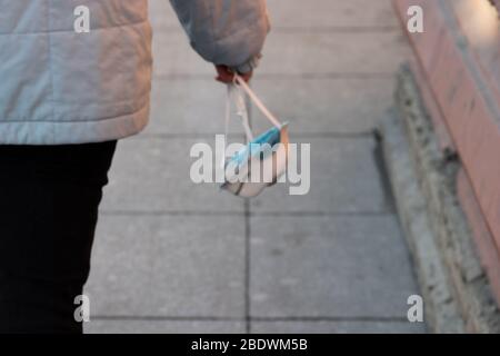 Eine Frau hält ein Atemschutzgerät in der Hand und geht die Straße entlang. Medizinische Schutzmaske gegen Viren, Infektionen und Bakterien. Kopierbereich Stockfoto