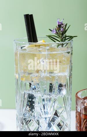 Gin Tonic Cocktail, mit Zitrone und blühendem Rosmarin, auf einem kleinen Tisch. Vintage-Ästhetik Stockfoto