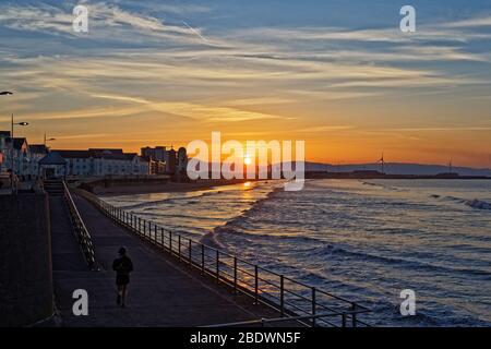 Die Sonne geht über Sanddünen und Kräne in Swansea Bay auf und markiert den Beginn eines weiteren warmen und sonnigen Tages in Südwales, Großbritannien. Mittwoch, 25. März 2020 Stockfoto