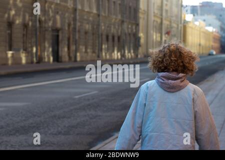 Mädchen mit lockigen blonden Haaren geht in der Stadt Straße in der Nähe der Straße. Kopierplatz im Freien. Foto von hinten Stockfoto