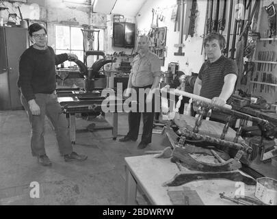 1980er Jahre, historisch, drei Möbelrestauratoren oder Restauratoren, die in ihrer Werkstatt stehen, die Wände sind mit Werkzeugen gesäumt und mit einem antiken Tisch und einem kleinen Hocker, der auf Reparatur und Restaurierung wartet, England, Großbritannien. Die Restaurierung alter und antiker Möbel ist ein Fachmann und Fachmann, da jedes Stück unterschiedliche Restaurierungsbedürfnisse hat. Stockfoto