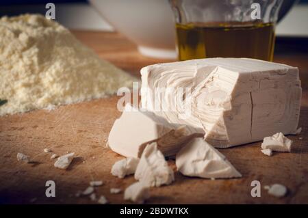 Ein Stock frischer Bierhefe, für Brot- und Pizzaäste verwendet, auf einem Holzbrett mit Mehl und Olivenöl Stockfoto