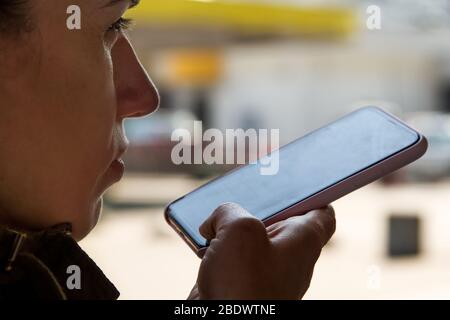 Eine Frau verwendet einen Sprachassistenten in ihrem Smartphone und diktiert Sprache mit Spracherkennungstechnologie. Das Konzept des Internets der Dinge. Stockfoto