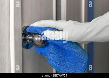 Hand des Mitarbeiters in Gummihandschuh mit Lappen, die eine Holztür abwischen. Zimmermädchen oder Hausfrau kümmert sich um das Haus. Allgemeine oder regelmäßige Reinigung der Feder. Com Stockfoto