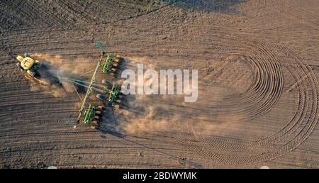 Frühlingsfeldarbeit, ein Traktor mit einem angebauten Säer sät Samen im Boden auf einem landwirtschaftlichen Feld. Luftaufnahmen. Stockfoto