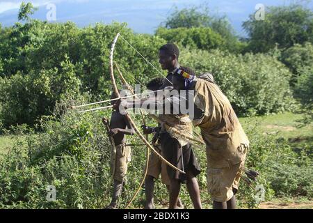 Hadza (Hadzabe) Mann, der während einer Jagdexpedition einen Pfeil auf einen Vogel abzielt. Hatzabe ist ein kleiner Stamm von Jägern Sammler in Ostafrika. Fotografiert Stockfoto