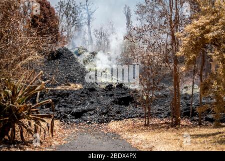 Das Haus wurde während des Vulkanausbruchs von Kīlauea, 19. Mai 2018, durch Lava zerstört. Beachten Sie die gelben Schwefelablagerungen, die sich um die Spalte bilden. Das Wohngebiet von Leilani Estates wurde aufgrund der hohen Konzentration von Schwefeldioxid evakuiert, das aus den Rissen in der Erde emittiert wurde, die Lava in die Unterteilungen verschüttete. Stockfoto