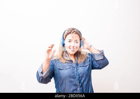 Glückliche blonde Frau, die Musik hört und die Kamera anschaut. Ihre linke Hand liegt auf ihrem Kopf. Stockfoto