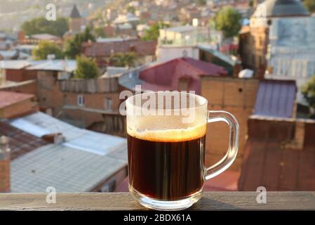 Machen Sie eine Tasse heißen Kaffee auf der Terrasse mit verschwommener Aussicht auf die Stadt im Hintergrund Stockfoto