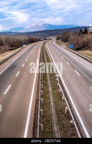 Mehrspurige, leere Autobahnstraße, die zu schneebedeckten Bergen führt Stockfoto