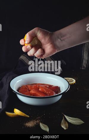 Salzen von roten Fischen. Männliche Hand drückt eine Zitrone in einer Schüssel mit Lachs. Stockfoto