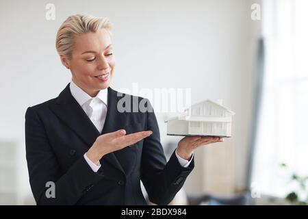 Reife Frau in schwarzem Anzug präsentiert das neue Modell des Hauses in den Händen Stockfoto