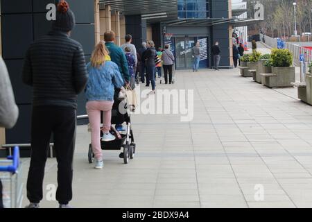 Lange Schlange von Käufern, die in sicherer Entfernung voneinander vor einem Tesco Supermarkt in Edinburgh stehen Stockfoto