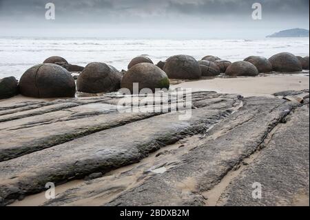 Die moeraki Boulders auf Koekohe Strand, Otago, Neuseeland. Felsenküste Formationen mit grauen bewölkten Himmel Hintergrund Stockfoto