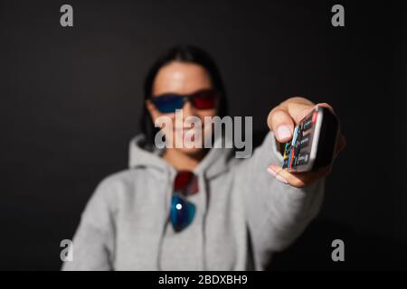 Porträt einer jungen Frau, die den Fernseher anschaltet und einen Film in einer 3D-Brille auf schwarzem Hintergrund anschaut Stockfoto