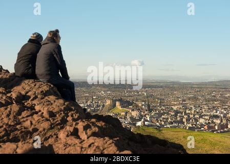 Ein Paar sitzt auf dem Arthurs Seat, einem schlafenden Vulkan, mit Blick auf die Stadt Edinburgh und Edinburgh Castle, Schottland. Stockfoto