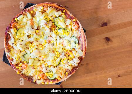 Hausgemachte vegetarische Veggie-Pizza mit Käse, Ananas, Mais, Gemüse, Zucchini, Blumenkohl auf Holztisch Stockfoto