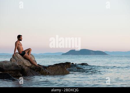 Junger Mann genießt Sonnenuntergang am Strand Stockfoto