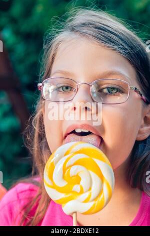 Kleines Mädchen in Gläser lecken große Lutscher Stockfoto