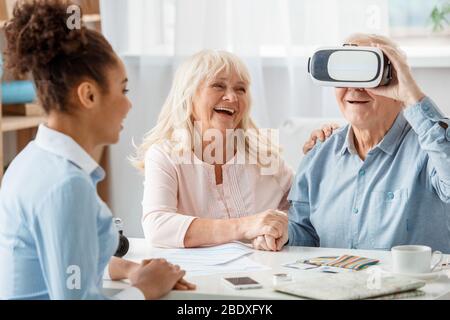 Reisebüro im Büro mit älteren Kunden Mann mit Virtual Reality-Headset lachend fröhlich Stockfoto