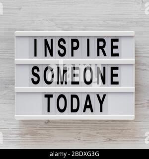 „Inspire someone today“-Worte auf einem Leuchtkasten auf einer weißen Holzfläche, Draufsicht. Über Kopf, von oben, flach gelegt. Stockfoto