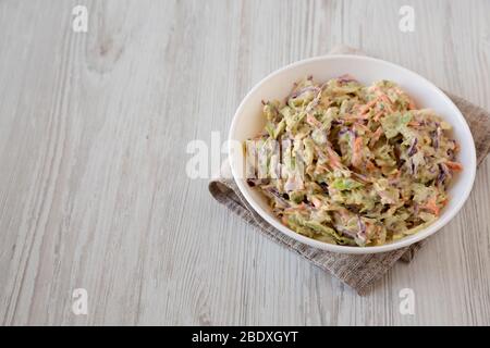 Selbstgemachte cremige Broccoli-Slaw in einer weißen Schüssel auf weißem Holzhintergrund, Seitenansicht. Kopierbereich. Stockfoto