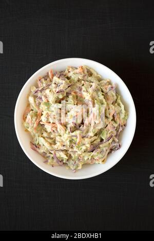 Selbstgemachte cremige Broccoli-Slaw in einer weißen Schüssel auf schwarzem Hintergrund, Blick von oben. Flach liegend, Ansicht von oben, von oben. Stockfoto