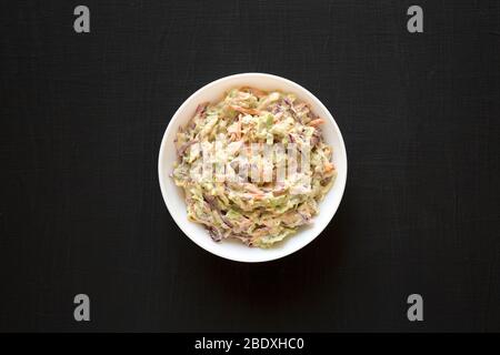 Selbstgemachte cremige Broccoli-Slaw in einer weißen Schüssel auf schwarzem Hintergrund, Blick von oben. Flach liegend, Ansicht von oben, von oben. Stockfoto