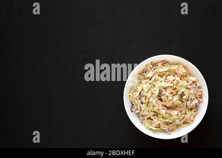 Selbstgemachte cremige Broccoli-Slaw in einer weißen Schüssel auf schwarzer Oberfläche, Draufsicht. Flach liegend, von oben, über Kopf. Stockfoto