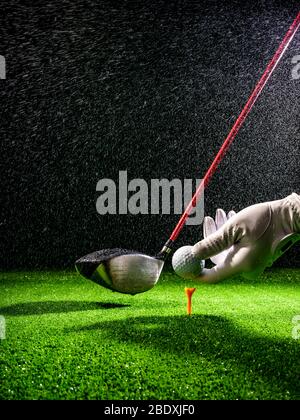 Hand, die einen Golfball auf dem Abschlag eines Golfplatzes im Regen setzt Stockfoto
