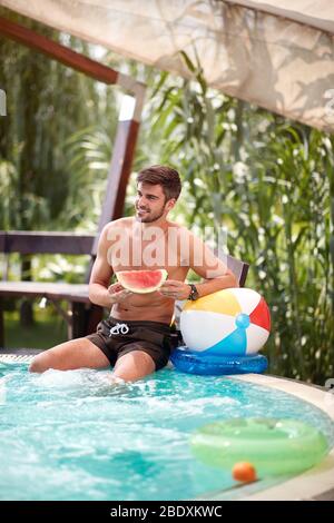 Junger Mann erfrischt sich im Swimmingpool draußen Stockfoto