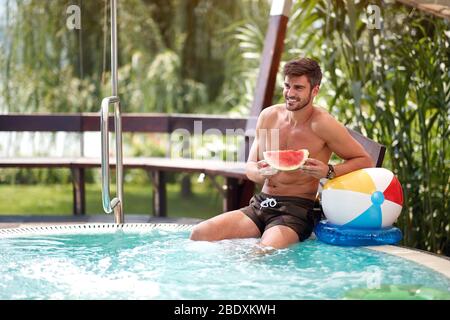 Männlich erfrischend im Schwimmbad mit Wassermelone Stockfoto