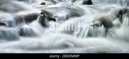 Wasserströme, die wunderschön einen wilden kleinen Fluss hinuntergehen, Panoramafenster und lange Belichtung für abstrakten Fluss Stockfoto