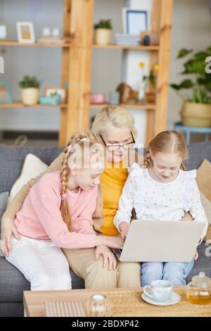 Großmutter, die mit ihren Enkelinnen auf dem Sofa sitzt und im Wohnzimmer einen Laptop benutzt Stockfoto