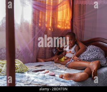 Kampala, Uganda - 15th. Juni 2017: Ein Porträt einer Afrikanerin mit ihrem Sohn, während sie am Nachmittag im Schlafzimmer auf einem Bett ruhten Stockfoto