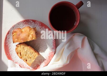 Frisch gebackener traditioneller Apfel-charlotte-Pudding in Backform und auf einem Teller mit Puderzucker. Leichter Kuchen und eine Tasse Tee zum Frühstück. Stockfoto