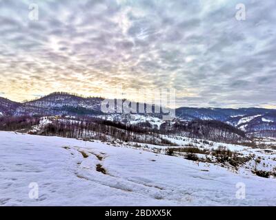 Landschaftlich reizvolle Berglandschaft mit schneebedeckten Hängen, schneebedeckten Berggipfeln und Wolken, die vom Sonnenuntergang in den Karpaten Rumäniens beleuchtet werden, beau Stockfoto