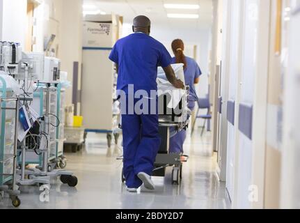NHS-Mitarbeiter schieben einen Patienten durch einen Krankenhauskorridor, der NHS steht unter großem Druck mit der Coronavirus-Pandemie. Stockfoto
