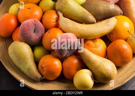 Sortierte ganze Früchte in großen Bambus-Obstschale - Foto von Birnen, flachen Pfirsichen, Orangen, Äpfeln und Bananen Stockfoto